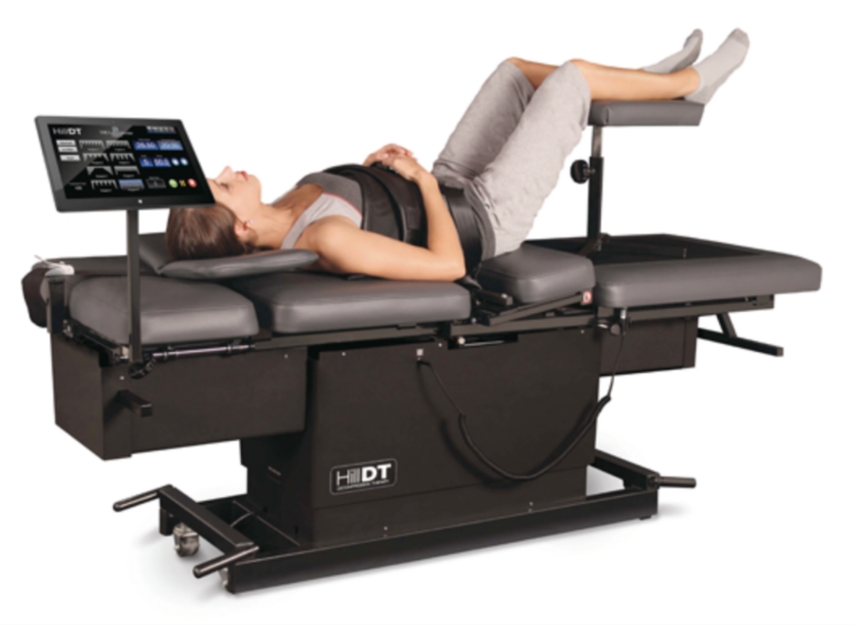 A woman lies on a spinal decompression table with a touchscreen, wearing gray activewear, for back therapy